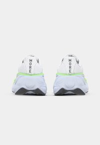 Rear view of white sneakers with lime green accents, featuring a textured upper, rounded sole, and "MORE" printed on the heel.