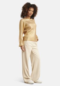 Gold ribbed sweater with long sleeves paired with loose cream-colored trousers. The outfit is complemented by white sneakers.