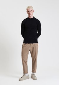 Maglietta nera attillata a maniche lunghe, tessuto leggero; pantaloni beige a gamba affusolata con zip laterali; sneaker beige con suole testurizzate.