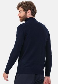 Pull bleu marine à manches longues et col montant, en texture douce, avec poignets et ourlet côtelés. Design minimaliste, sans motifs ni accents visibles.