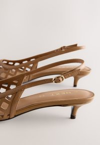 Sandales à talon kitten en cuir marron avec bride arrière, design ajouré et petite boucle dorée sur fond neutre.