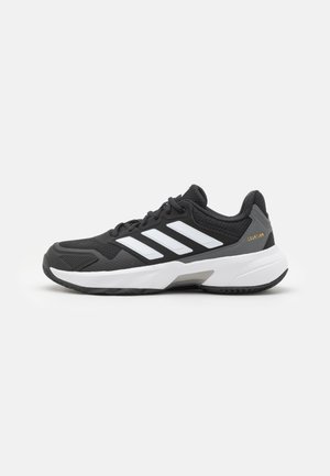 Zapatilla deportiva negra con rayas blancas, malla texturizada y material sintético, con suela de goma y un acento gris en el talón.