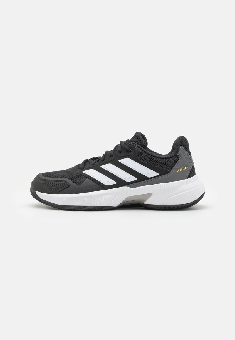 Chaussure de sport noire avec des rayures blanches, en mesh texturé et matériau synthétique, dotée d'une semelle en caoutchouc et d'un accent gris au niveau du talon.