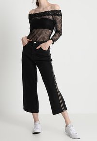 Musta pitsinen toppi ilman olkaimia mustan bandeaun päällä, yhdistettynä leveälahkeisiin mustiin farkkuihin, joissa on valkoiset sivuviivat, sekä valkoisiin tennareihin.