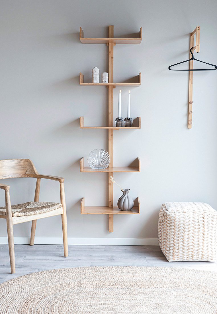 Étagère en bambou avec cinq étagères rectangulaires, portant divers objets de décoration. Chaise en bois clair et tapis texturé complètent le design minimaliste.