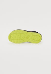 Svart sandal bunn med en tykk, teksturert limegrønn såle, som har et mønster og "Teva"-logoen i midten.