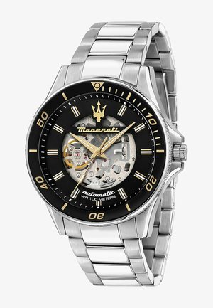 Zilveren roestvrijstalen automatische horloge met een zwarte wijzerplaat, skeletontwerp, gouden accenten en een metalen schakelarmband. Waterbestendig tot 100 meter.