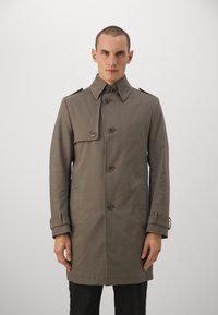 Cappotto khaki con design doppiopetto, spalline, bottoni frontali e tasche laterali. Realizzato in un tessuto liscio e testurizzato.