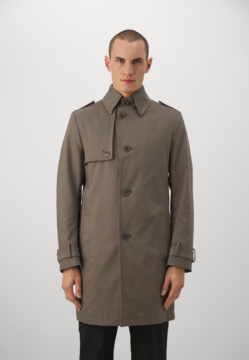 Cappotto khaki con design doppiopetto, spalline, bottoni frontali e tasche laterali. Realizzato in un tessuto liscio e testurizzato.