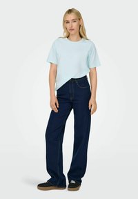 Lyseblå t-shirt med korte ærmer kombineret med højtaljede mørkeblå denimbukser. Overtøjet har lige ben og minimal detaljering.