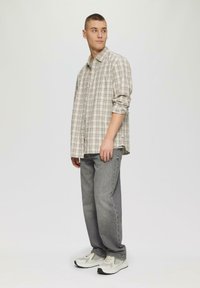 Bordeaux geruit shirt in beige en grijs, met knopen en opgerolde mouwen. Grijze jeans en lichte sneakers met zichtbare textuur en patroondetails.
