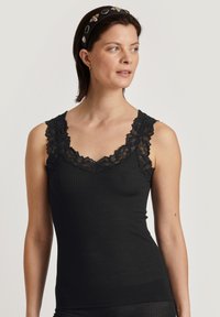Top a maniche corte nero a costine con scollatura a V, caratterizzato da un elaborato profilo in pizzo nero sulle spalle. Tessuto morbido con silhouette aderente.
