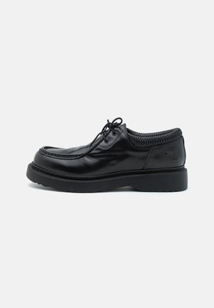 Black leather shoes with a round toe and a thick rubber sole. Features a braided collar and curved stitching along the upper.
