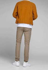Veste en velours côtelé moutarde, pantalon beige ajusté, et baskets blanches. La vue arrière montre les détails de couture et une coupe décontractée.