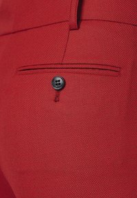 Czerwony tkanina o teksturze z gładkim wykończeniem, z czarnym guzikiem na kieszeni, podkreślona drobnymi detalami szwów.