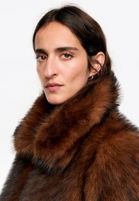 Brązowy futrzany kołnierz o miękkiej, puszystej teksturze, z ciemnym podkładem. Zbliżenie ukazuje cechy twarzy i ciepłe, brązowe oczy.