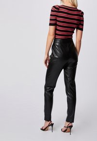 Pantalon en cuir noir à coupe slim, associé à un haut ajusté à rayures rouges et noires. Des talons ouverts noirs complètent la tenue.