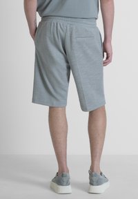 Pantaloni corti grigi con una cintura elastica, dotati di una tasca posteriore. Abbinati a scarpe grigie, mostrati da una vista posteriore.