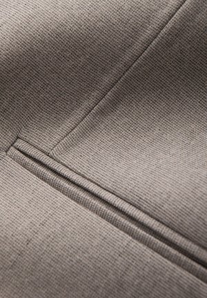 Grå texturerad tyg med ett subtilt rutmönster, med synlig sömnad och en elegant fickdetalj på ytan.