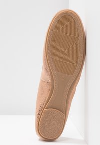 Chaussure marron clair avec un dessus perforé, une semelle texturée et un design flexible. Taille indiquée comme 37 sur la semelle.