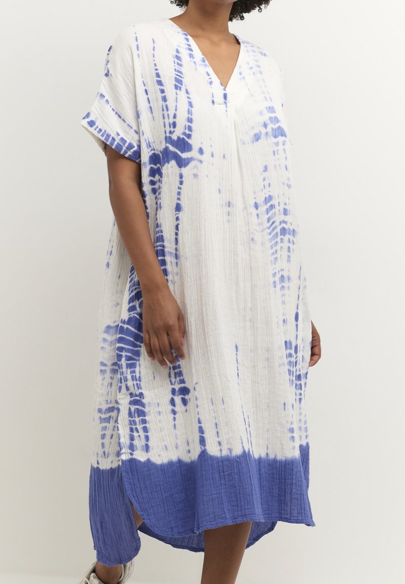 Vit och blåmönstrad klänning med V-ringning, korta ärmar och ett strukturerat tyg. Har en längre bakre kant och sidofunktioner.