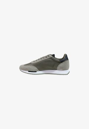 Lage sportieve schoen in groen en grijs suède en stof met een witte getande zool, gezien van opzij tegen een witte achtergrond.