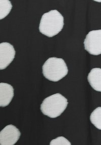 Tissu noir avec de grands pois blancs espacés de manière uniforme, chaque point étant légèrement irrégulier en forme et aux bords doux.