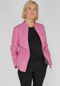 Rosa Lederjacke mit Reißverschluss, taillierter Passform und seitlichen Taschen. Über einem schwarzen Oberteil getragen, kombiniert mit schwarzen Hosen. Glatte Textur.
