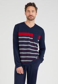 Marineblauwe V-hals shirt met lange mouwen, voorzien van horizontale strepen in rood en grijs, met een zakje op de linkerborst, gemaakt van een zachte stof.