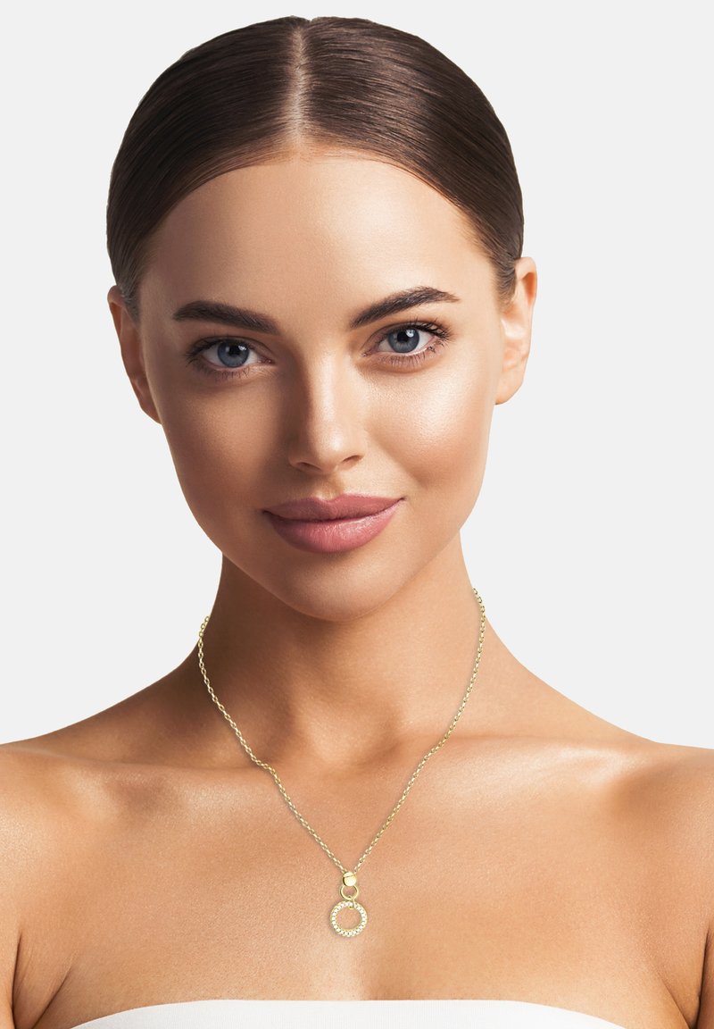Goldene Halskette mit einer zarten Kette und einem kreisförmigen Anhänger, der ein dekoratives Ringdesign aufweist. Glatte Textur mit einem glänzenden Finish.
