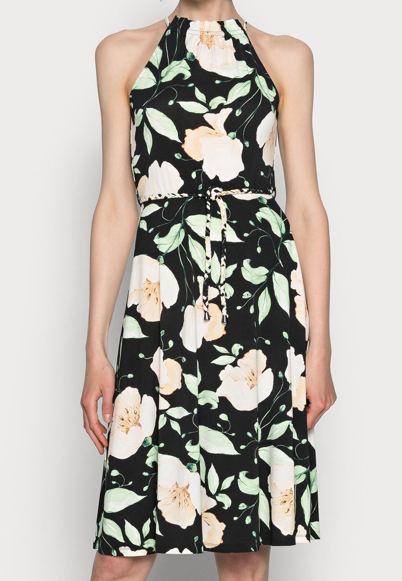 Robe noire sans manches avec encolure halter, présentant un grand motif floral blanc et pêche pâle ainsi qu'une fine ceinture tressée à nouer à la taille.