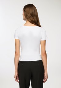 Top corto a maniche corte bianco a costine con scollatura rotonda, abbinato a pantaloni neri con tasche posteriori e accentuazioni a bottoni.