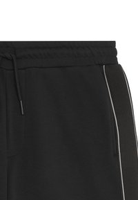 Pantaloni sportivi neri realizzati in tessuto morbido, caratterizzati da una vita con cordino, tasche laterali e strisce grigie a contrasto lungo i lati.