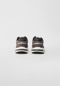 Un paio di sneakers Armani Exchange marroni e grigie viste da dietro su uno sfondo bianco.