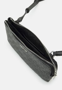 Černá texturovaná kabelka na zip, s hladkým vnitřním prostorem, odnímatelným popruhem a kovovým logem.