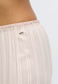 Pantaloni a righe beige con tessuto leggero, vita elasticizzata e piccolo logo 'BOSS' in argento vicino alla vita. Sottili accenti rosa e blu.