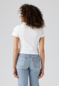 Λευκή μπλούζα κοντομάνικη με εφαρμοστό μέσο, σε συνδυασμό με ανοιχτό μπλε τζιν που διαθέτει ιδιαίτερο σχέδιο ραφής στις πίσω τσέπες.