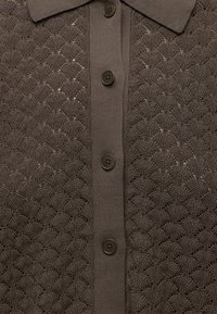 Cardigan marron tricoté avec un motif festonné, un col à revers et cinq boutons sombres sur le devant au centre.