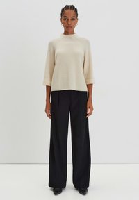 Top di maglia a coste beige con collo alto e maniche a tre quarti, abbinato a pantaloni neri a gamba larga e scarpe nere con punta.