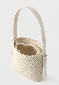 Beżowa torebka o splocie z ustrukturyzowanym kształtem, wyposażona w kremową podszewkę wewnętrzną oraz gładki skórzany pasek z otworami do regulacji.