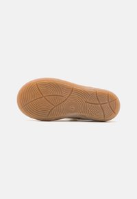 Suela de zapato de goma con un patrón texturizado y ondulado en marrón claro, que presenta surcos y curvas para ofrecer agarre y tracción. Número "25" visible.