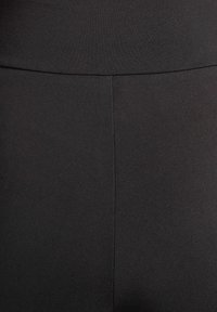 Zwarte legging gemaakt van rekbare stof, met een gladde textuur en een hoge tailleband. Zichtbare naad aan de voorkant.