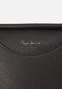 Bolsa de cuero negro con una superficie texturizada. Presenta una solapa redondeada y el logotipo plateado "Pepe Jeans London" destacado.