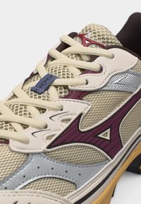 Pantof sport cu plasă bej, suprapuneri bordo și argintii, șireturi crem și talpă cărămizie, cu logo-ul Mizuno pe lateral și pe limbă.