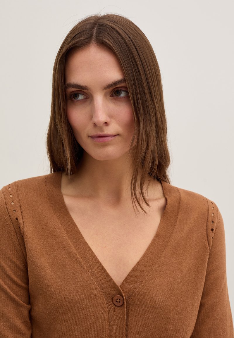 Brauner Strickcardigan mit V-Ausschnitt, ausgestattet mit einer Knopfleiste und dekorativen Nähten an den Ärmeln. Weicher Stoff, figurbetontes Design.