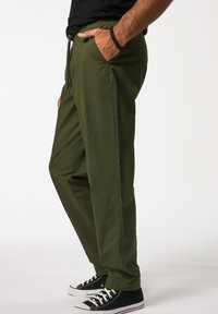 Olivgrüne Hose mit elastischem Bund, Seitentaschen und lockerer Passform, kombiniert mit schwarzen High-Top-Sneakern.