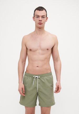 Shorts de bain vert clair en tissu léger avec une taille élastique et un cordon blanc. Texture lisse et longueur jusqu'aux genoux.