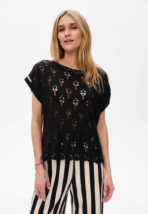 Black knitted top featuring a detailed openwork pattern, short sleeves, and a loose fit, paired with striped black and white trousers.