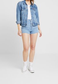 Ljusblå denimjacka med frontfickor, kombinerad med högmidjade blå leopardmönstrade shorts. Modellen bär vita högskurna sneakers.