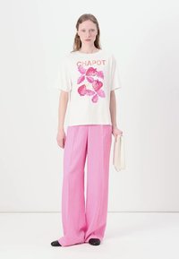 Witte T-shirt met een roze aardbei graphic en "CHAPOT" tekst, gecombineerd met lichtroze, wijde broek en zwarte schoenen.